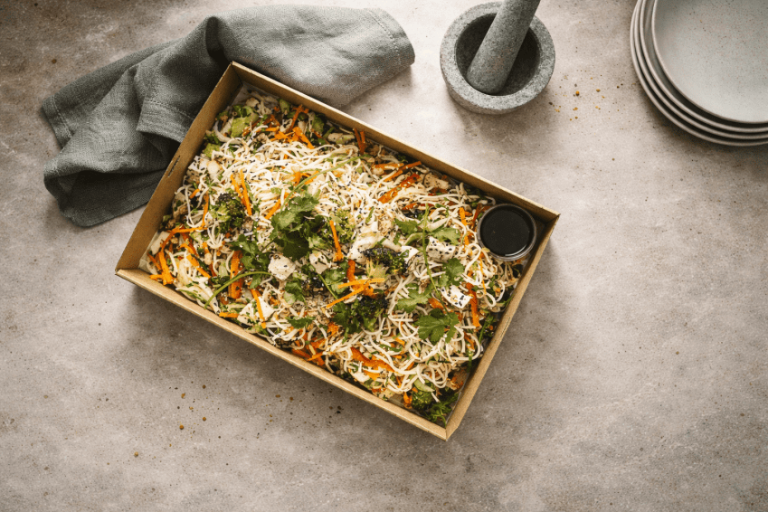 A shared catering box filled with a colourful noodle salad and dressing.