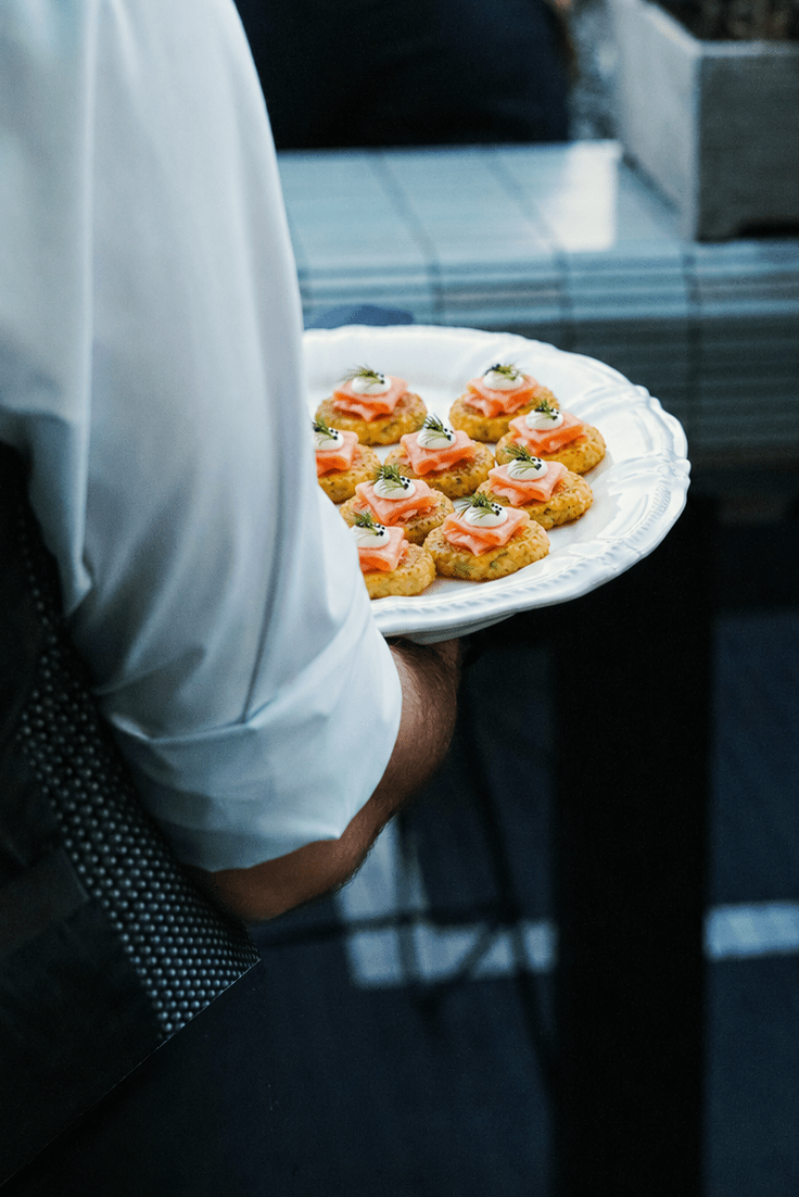 A waiter presenting freshly prepared corn fritters for a private event.